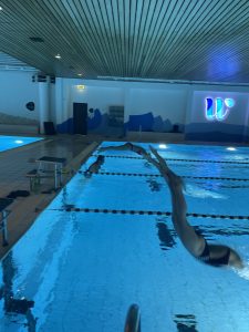 Schwimmer in einer Bahn im blau beleuchteten Hallenbad.