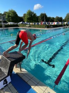 Schwimmer in roter Badebekleidung beim Absprung im Freibad.