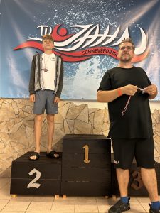 Teilnehmer mit Medaille vor dem Podest; dahinter eine weitere Person.