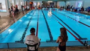 Blick längs über die Schwimmbahnen mit Personen am Beckenrand.