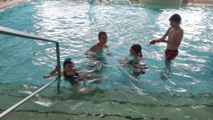 Vier Kinder im Wasser neben dem Einstiegsbereich des Beckens.