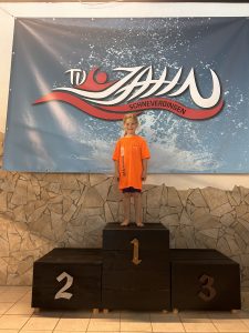 Kind im orangefarbenen Shirt auf Platz eins vor dem Vereinsbanner.