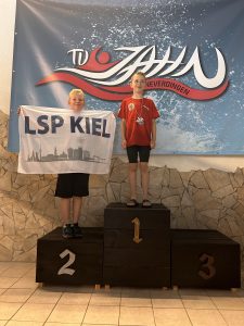 Zwei Teilnehmende auf dem Podest mit einem Schild mit der Aufschrift LSP Kiel.